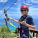 A boy posing on a platform while tethered to a zip line pulley with the coastline behind him